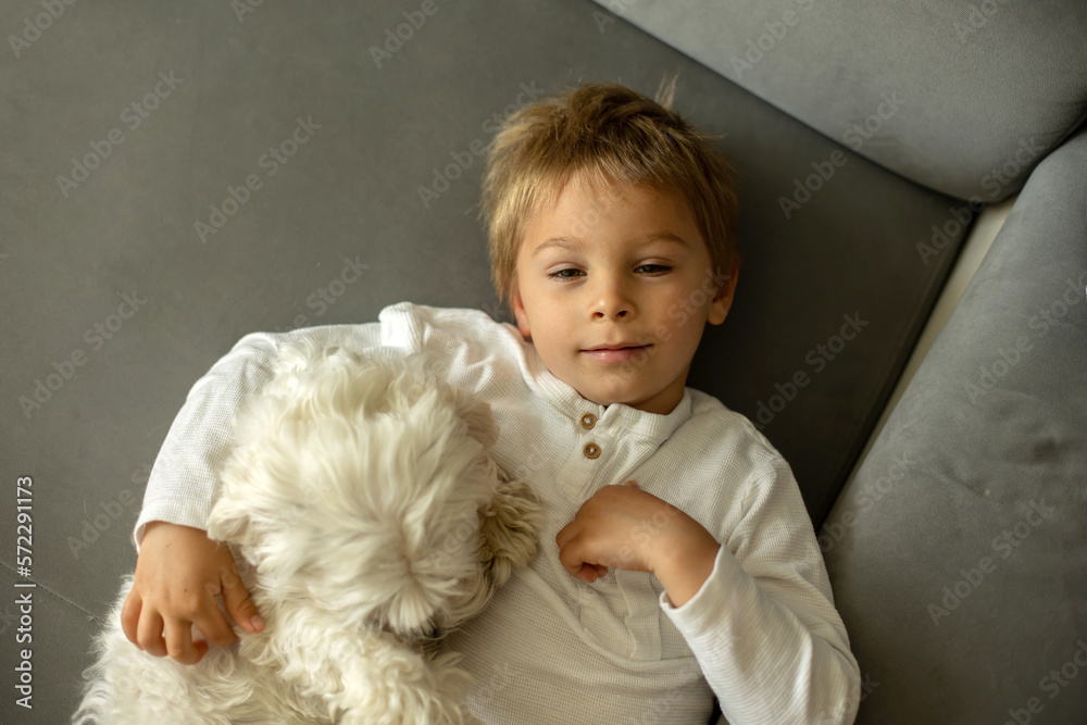Cute blond child, toddler boy, lying on the couch with his pet dog Cute blond child, toddler boy, lying on the couch with his pet dog
