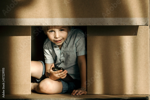 Cute toddler child and maltese pet dog, hiding in cardboard box, playing