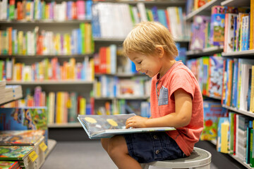 Cute preschool child, looking at books in a bookstore on summer day