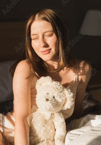 Girl is waking up in morning stretches in bed and sun shines from the window. Happy young woman greets new sunny day