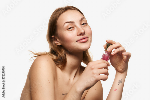 Happy young beautiful girl with long blonde hair holding moisturizing lotion, serum for face skin. Model with bare shoulders. Concept of skin care, beauty, anti-aging procedures.