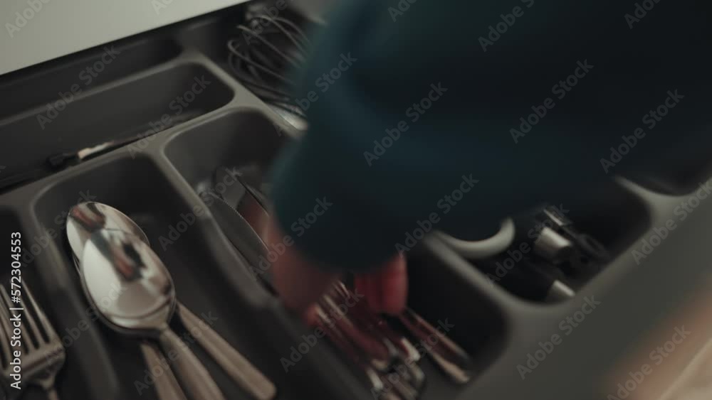 Frau räumt Löffel aus der Spülmaschine in die Besteck Schublade ein.