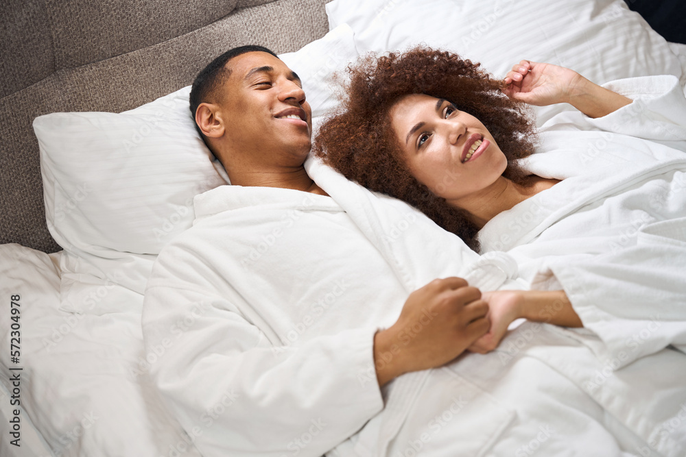 Fototapeta premium Beautiful multiracial couple lies on the bed in hotel room