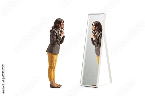 Full length profile shot of a young woman getting ready in front of a mirror and putting a scarf