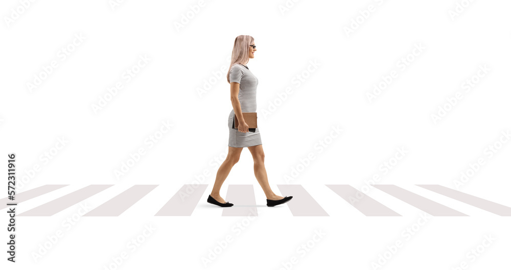 Full length profile shot of a woman holding books and walking on a pedestrian crossing