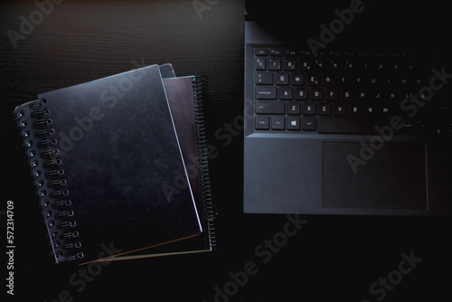 Over View of a office table with a black laptop and black 
notebooks.