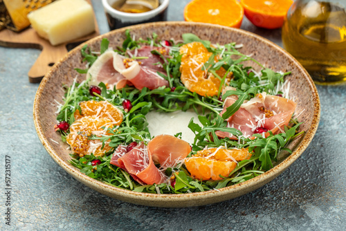 plate of arugula salad with mandarins, prosciutto jamon and Parmesan cheese on a light background. banner, menu, recipe place for text, top view