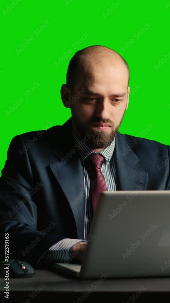 Vertical video: Executive manager using laptop over green screen backdrop, using computer at desk. Confident corporate employee posing on blank chroma key template, isolated copyspace background. Vertical video: Executive manager using laptop over green screen backdrop, using computer at desk. Confident corporate employee posing on blank chroma key template, isolated copyspace background.