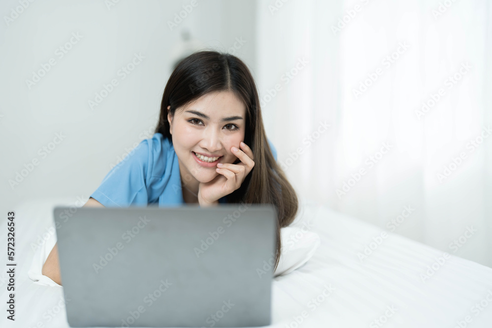 Happy, Relaxing Young beautiful Asian female watching movie or series on notebook in emotional smile happily while laying on the bed in her bedroom. Day off, Chill out and leisure concept. Happy, Relaxing Young beautiful Asian female watching movie or series on notebook in emotional smile happily while laying on the bed in her bedroom. Day off, Chill out and leisure concept.