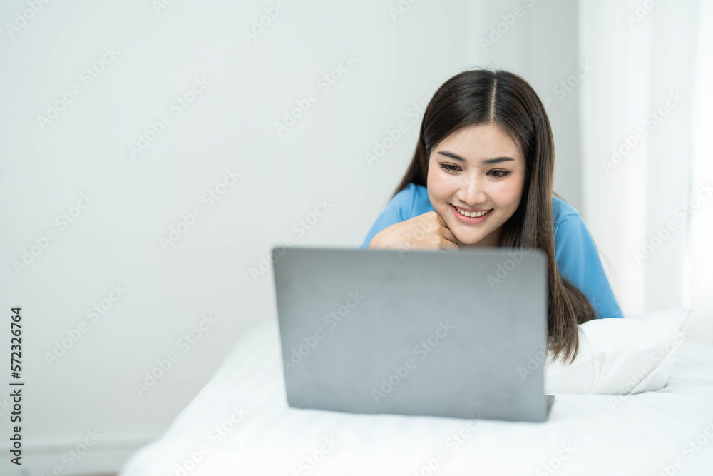 Happy, Relaxing Young beautiful Asian female watching movie or series on notebook in emotional smile happily while laying on the bed in her bedroom. Day off, Chill out and leisure concept. Happy, Relaxing Young beautiful Asian female watching movie or series on notebook in emotional smile happily while laying on the bed in her bedroom. Day off, Chill out and leisure concept.