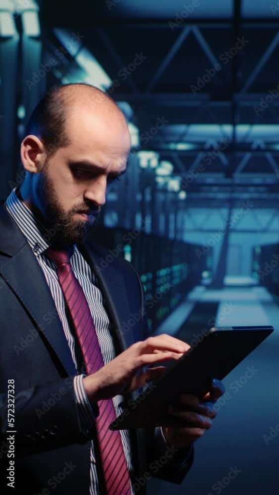 Vertical video: IT engineer using tablet in high tech server room, planning networking computer system. Database admin activating hardware server in data center, mainframe computer processor storage. Vertical video: IT engineer using tablet in high tech server room, planning networking computer system. Database admin activating hardware server in data center, mainframe computer processor storage.