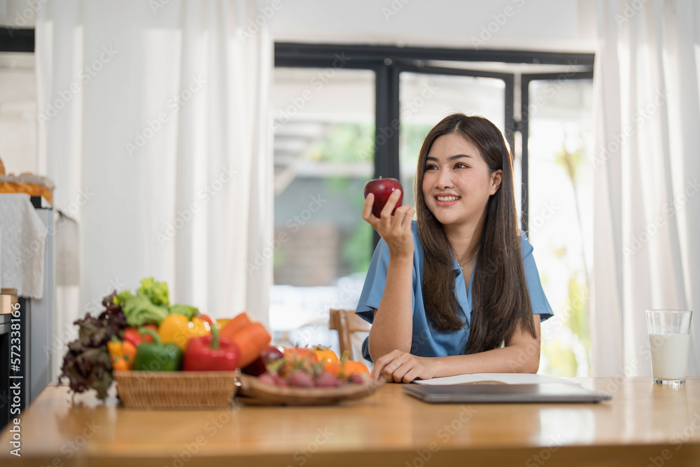 Beautiful young asian woman working on laptop computer while sitting at the kitchen room background.