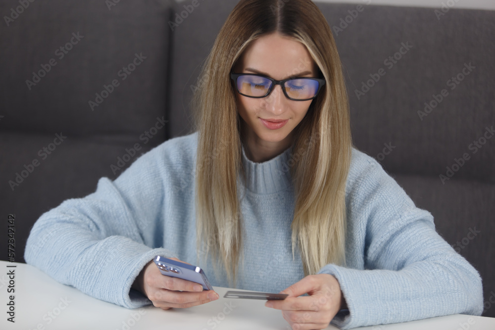 Woman shopping online with credit card and mobile phone. Portrait of beautiful blonde female making a payment in app on a smart phone