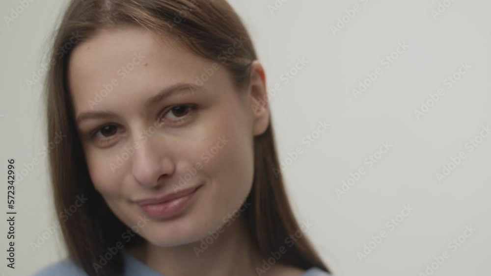 Smiling brunette woman looks at the camera and tucks her hair behind her ear. Portrait shooting in the studio on a white background. Smiling brunette woman looks at the camera and tucks her hair behind her ear. Portrait shooting in the studio on a white background.