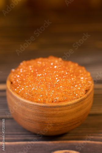 Red caviar in a ceramic cup on a wooden background . A place for advertising, logo, label, layout, mock-up.