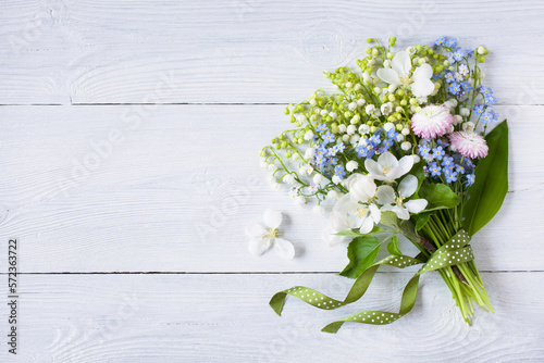 Bouquet of spring lilies of the valley, forget me not, flowers, daisies, apple blossoms and ribbon on white wooden background, copy space