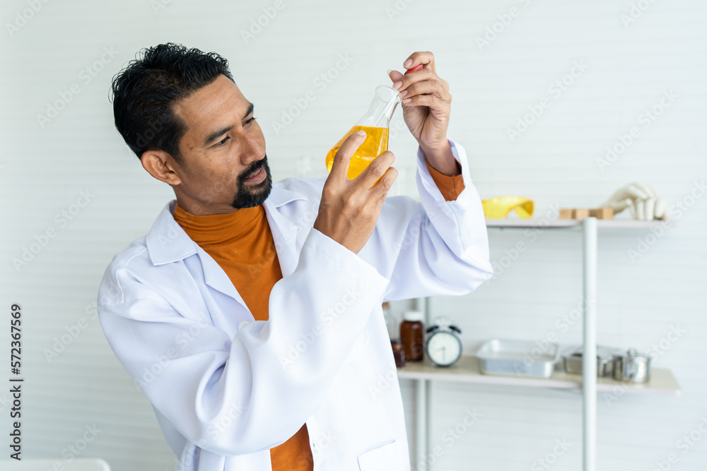 Male teacher in white lab coat using pipette bare hand carefully transfer chemical liquid in yellow flask required volume thoroughly with laboratory tools background in university classroom. Male teacher in white lab coat using pipette bare hand carefully transfer chemical liquid in yellow flask required volume thoroughly with laboratory tools background in university classroom.