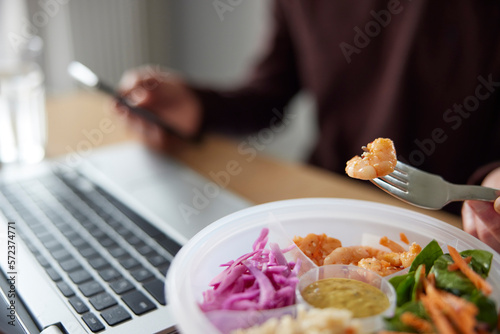 Close Of Man Eating Healthy Lunch At Office Deak Whilst Using Laptop