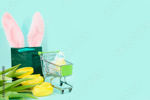 Easter eggs in a grocery basket on a blue background with yellow tulips and a paper bag. easter, shopping. High quality photo