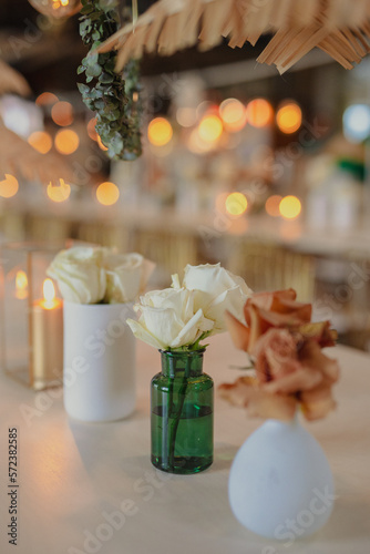 A delicate arrangement of white and orange roses in modern vases, set on a table with warm ambient lighting.