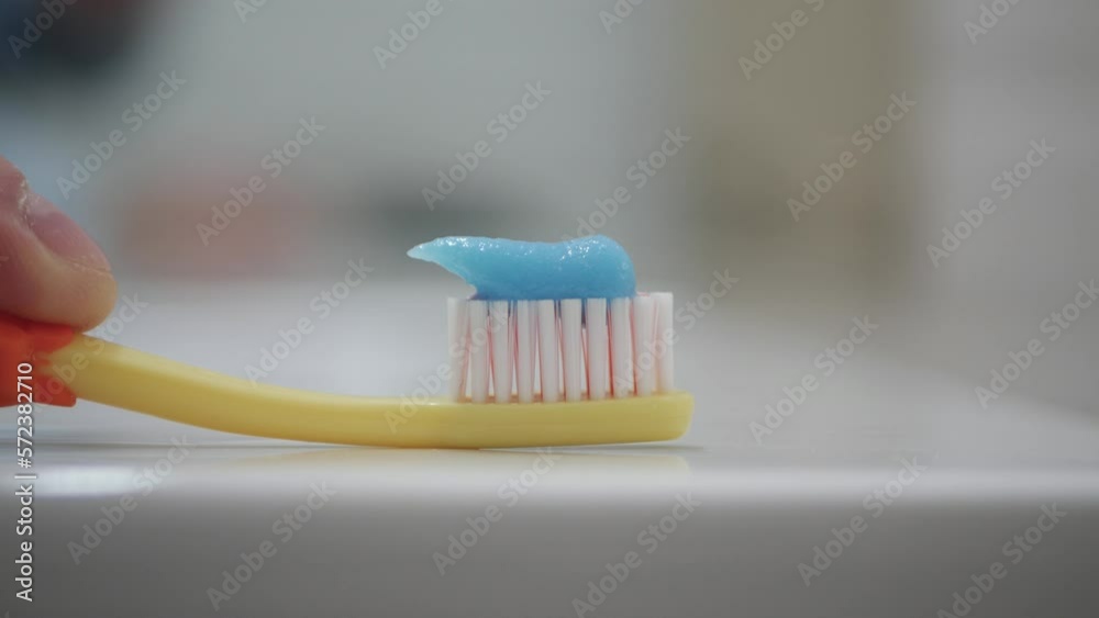 Close-Up Shooting with a Person in the Bathroom Putting Toothpaste on a Toothbrush. Daily and Healthy Routine for Tooth Cleaning. Close-Up Shooting with a Person in the Bathroom Putting Toothpaste on a Toothbrush. Daily and Healthy Routine for Tooth Cleaning.
