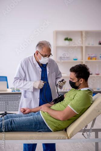 Old male doctor measuring young patient's blood pressure