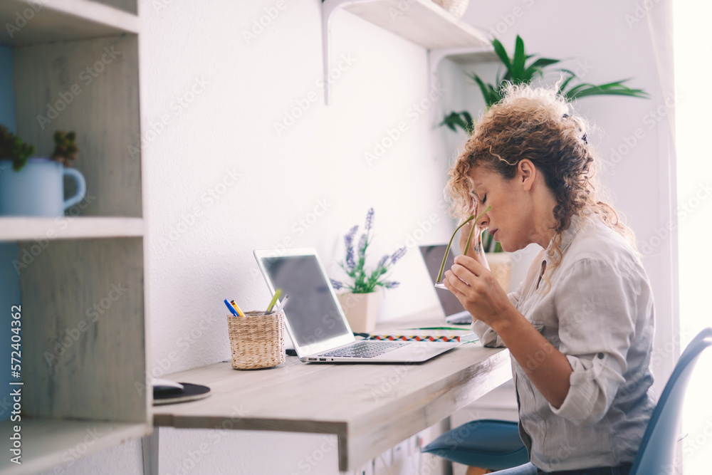 Obraz premium Tired stressed middle age business woman suffering from neckpain working from home office sitting at table. Overworked adult lady massaging neck feeling hurt pain from incorrect posture. Lifestyle