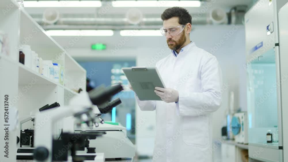 Portrait of concentrated mature man scientist with protective glasses and gloves working make notes descriptions and looking at the camera at microbiology pharmaceutical biochemistry laboratory indoor Portrait of concentrated mature man scientist with protective glasses and gloves working make notes descriptions and looking at the camera at microbiology pharmaceutical biochemistry laboratory indoor
