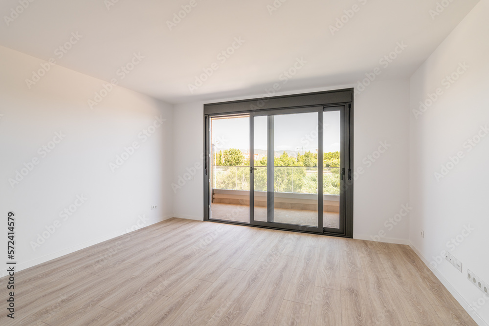 Spacious large room with wooden parquet structure and panoramic window overlooking beautiful landscape among complex of new buildings and balcony with elegant glass border. Mortgage and moving concept Spacious large room with wooden parquet structure and panoramic window overlooking beautiful landscape among complex of new buildings and balcony with elegant glass border. Mortgage and moving concept