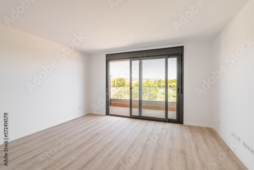 Fotografia Spacious large room with wooden parquet structure and panoramic window overlooking beautiful landscape among complex of new buildings and balcony with elegant glass border