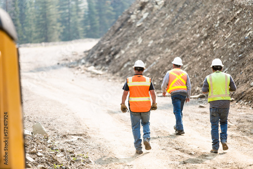 Three construction workers walking down a dirt road on a job site
