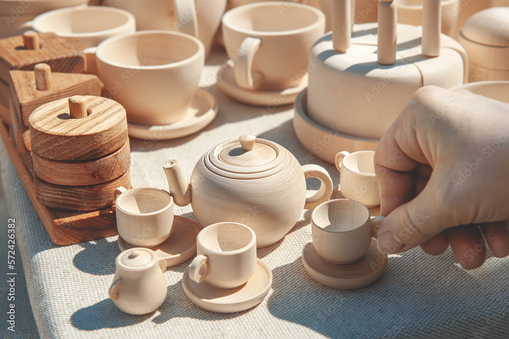 hand takes the cup. wooden teapot with cups. various wooden toys as a gift, eco-friendly and safe handmade products for the development and education of children hand takes the cup. wooden teapot with cups. various wooden toys as a gift, eco-friendly and safe handmade products for the development and education of children