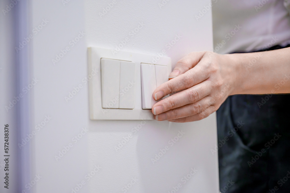 A woman turns off the home light switch when she leaves the room. Power, energy saving, energy saving.