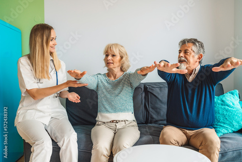Fototapeta Naklejka Na Ścianę i Meble -  Woman caregiver assisting senior couple at nursing home, showing them some exercises 