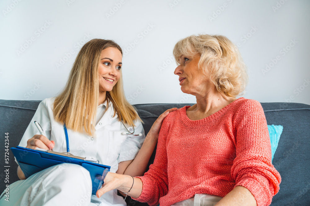 Caregiver helping elderly lady at home, both of them sitting on the couch talking Caregiver helping elderly lady at home, both of them sitting on the couch talking