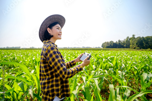 Asian female farmer in striped shirt piloting a drone at a corn field.