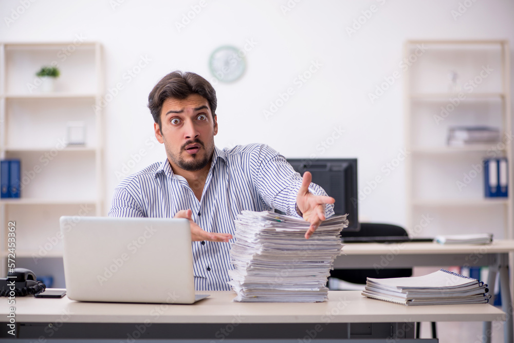 Young male employee and too much work in the office Young male employee and too much work in the office