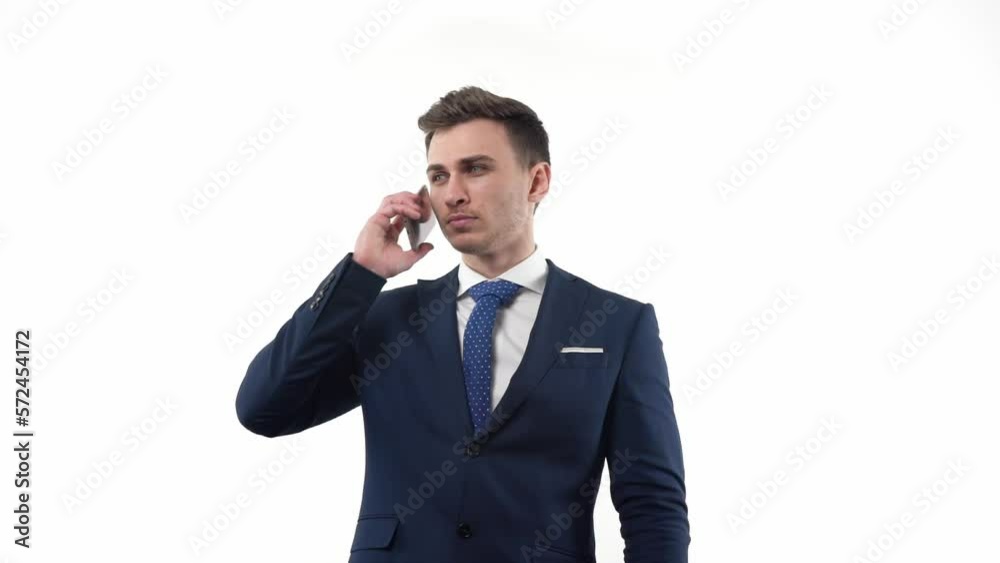 A young male businessman in a suit answers a call on a smartphone and has a business conversation. In the studio on a white background. A young male businessman in a suit answers a call on a smartphone and has a business conversation. In the studio on a white background.