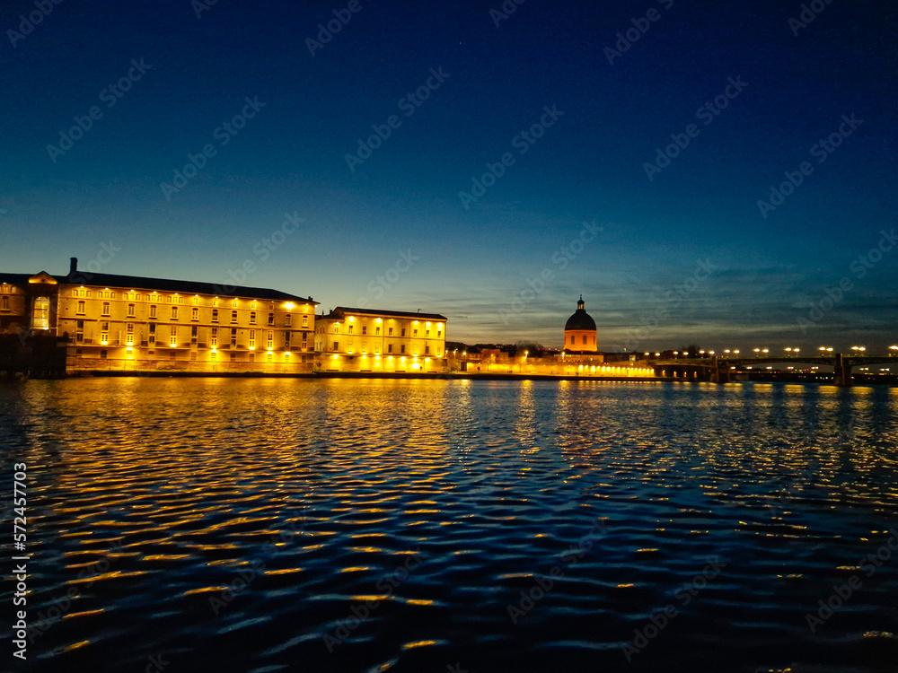a panoramic view of the garonne river passing through saint pierre bridge with  la grave hospital in the background at night. Toulouse. Light reflection on the garonne river