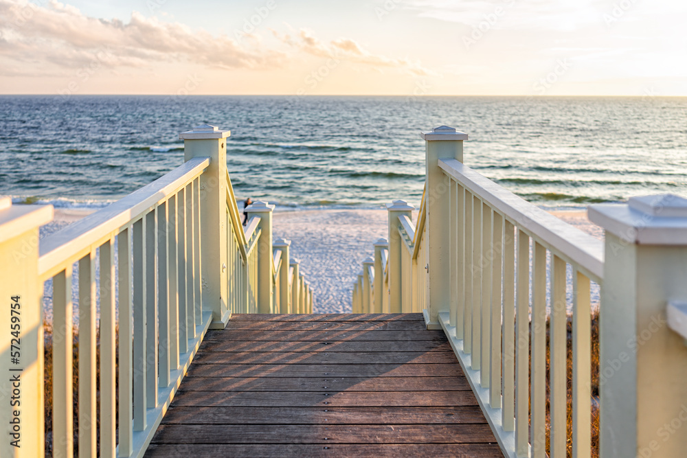 Fototapeta premium High angle framing view of wooden yellow green white pavilion boardwalk railing stairs steps leading to beach at Gulf of Mexico in Seaside, Florida panhandle sunset and nobody
