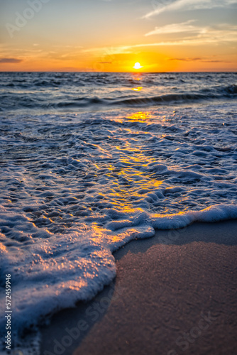 Ground level low angle view closeup of colorful vertical sunset in Gulf of Mexico coast with water wave in Seaside Santa Rosa Beach, Florida panhandle and reflection