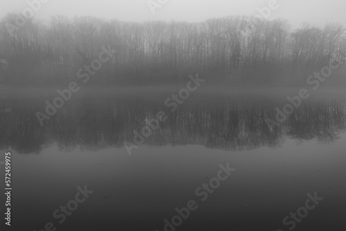 Black and white image of fog covering lake and trees