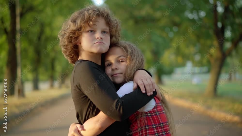 Loving couple of children hugging standing on park alley at sunset on spring summer day. Side view portrait of relaxed happy Caucasian girl and boy embracing outdoors in sunshine Loving couple of children hugging standing on park alley at sunset on spring summer day. Side view portrait of relaxed happy Caucasian girl and boy embracing outdoors in sunshine