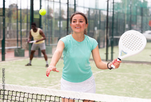 Young adult woman playing doubles padel game with male partner at warm sunny day, healthy lifestyle concept © JackF