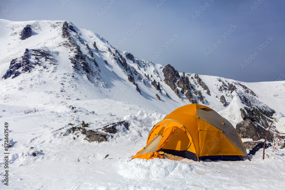 Hikers set orange tent in winter mountains. Alpinism sport