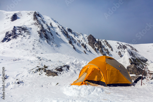 Hikers set orange tent in winter mountains. Alpinism sport