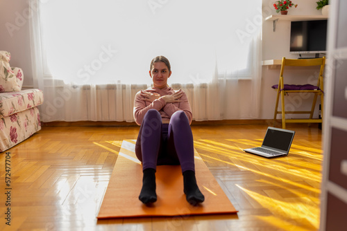 Online workout. Teen girl doing Sport exercise at home, watching tutorials on a laptop. How to keep fit indoors