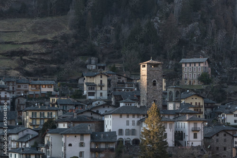 Little village of Gromo, Lombardy, Italy - February 2023. The last rays of the setting sun illuminate the village