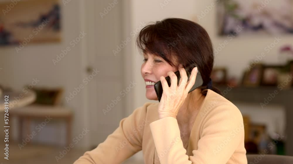 Closeup profile attractive middle age woman long hair earrings smiling talking business on mobile phone sitting at dining table in leisure home