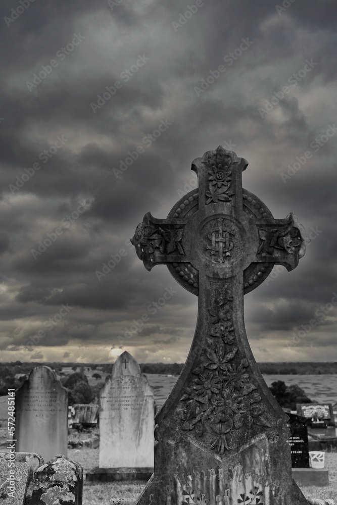 Black and white Celtic cross tombstone of a Christian grave in a cemetary with a stormy sky.